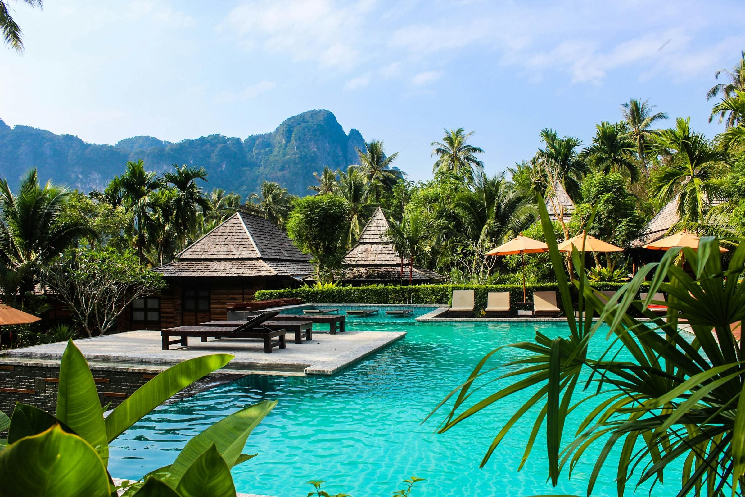 Turquoise pool among palms and Thai-style pavilions below limestone cliffs in Ao Nang