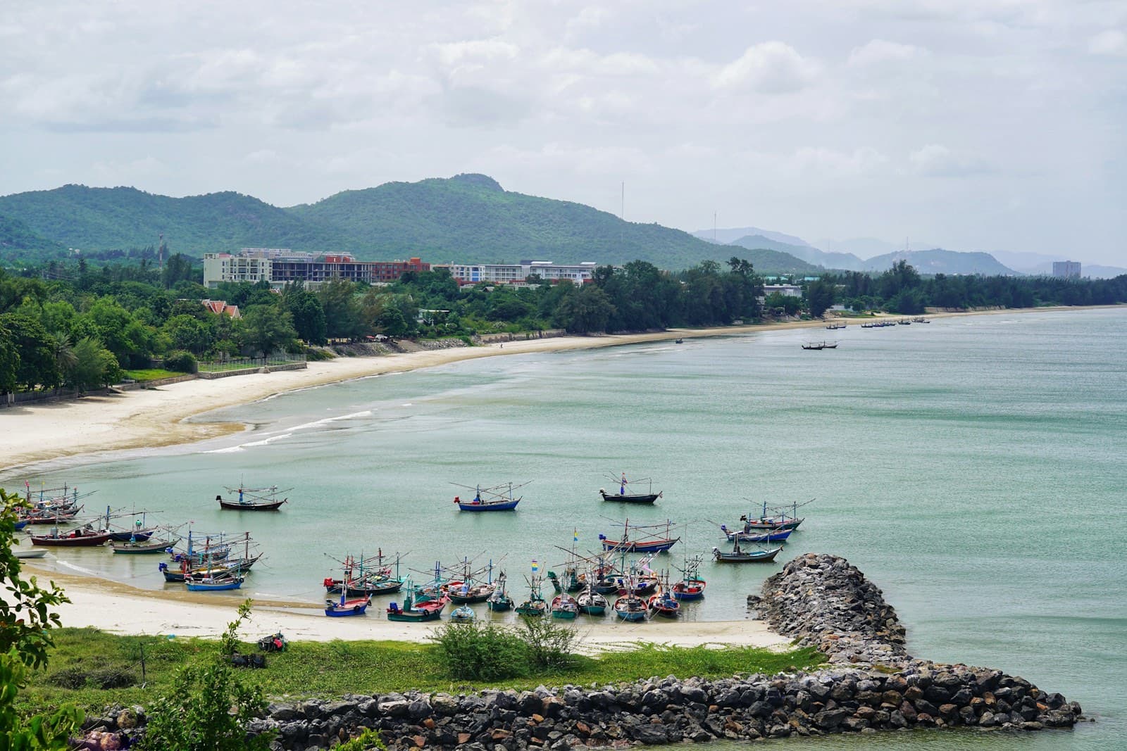 Fishing boats moored in the calm bay at Khao Tao beach, Hua Hin, with green hills behind