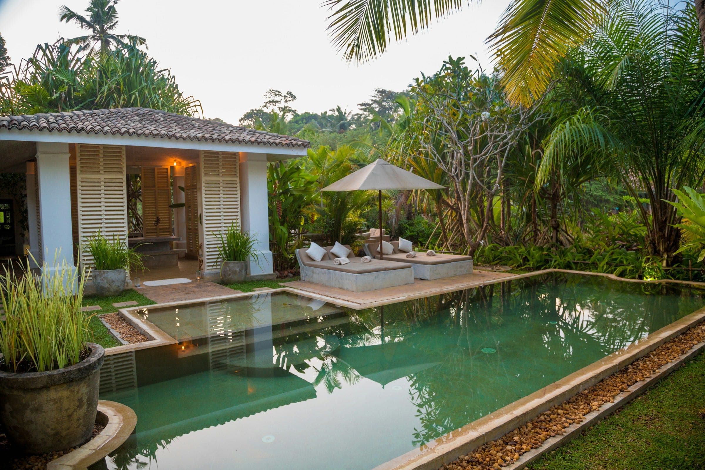 Shuttered garden pavilion beside a reflecting pool surrounded by lush tropical planting